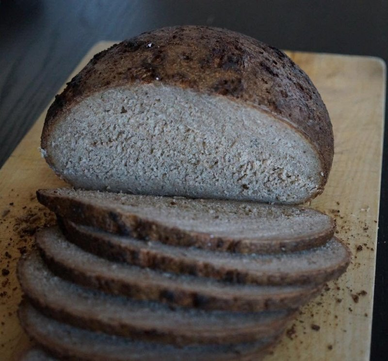 Auto-generated description: A loaf of dark bread is partially sliced on a wooden cutting board.