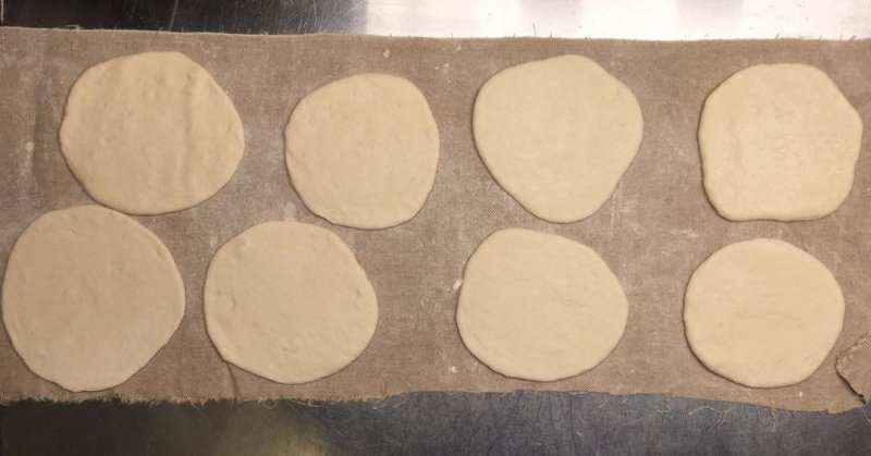 Auto-generated description: Eight circles of dough are arranged in two rows on a cloth-covered surface.