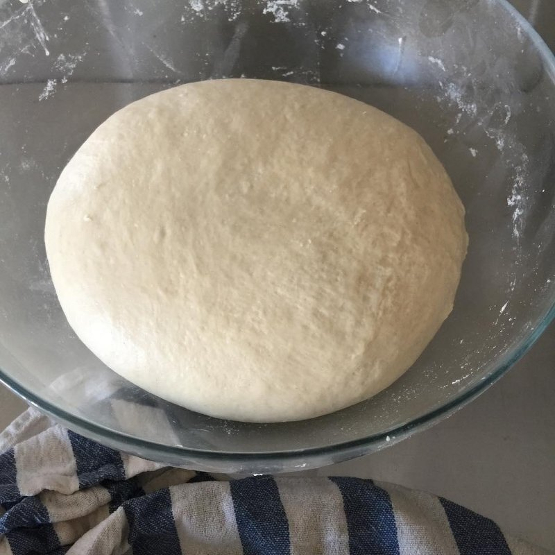 Auto-generated description: A round ball of dough rests in a clear glass bowl on a striped cloth.