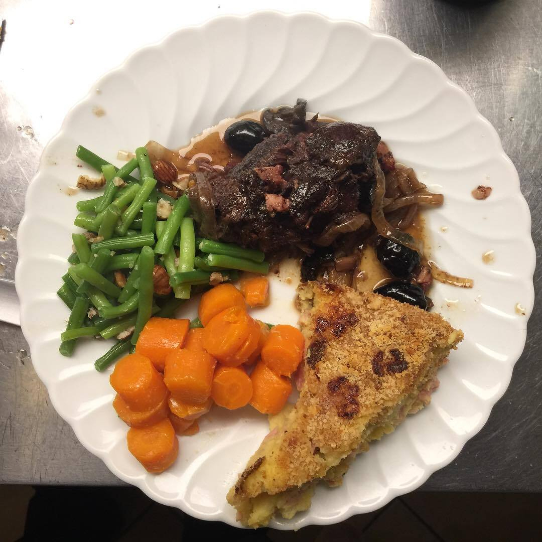 Beef stew, carrots, green beans and potatoes on a white plate.