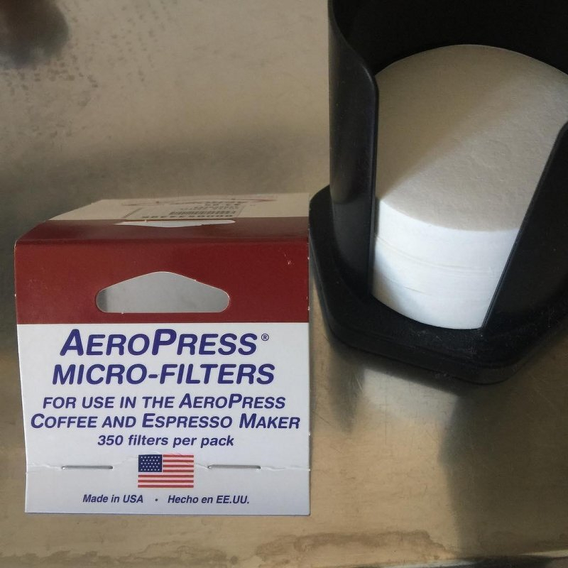 Auto-generated description: An empty box of Aeropress micro-filters is shown next to a black holder containing more filters.
