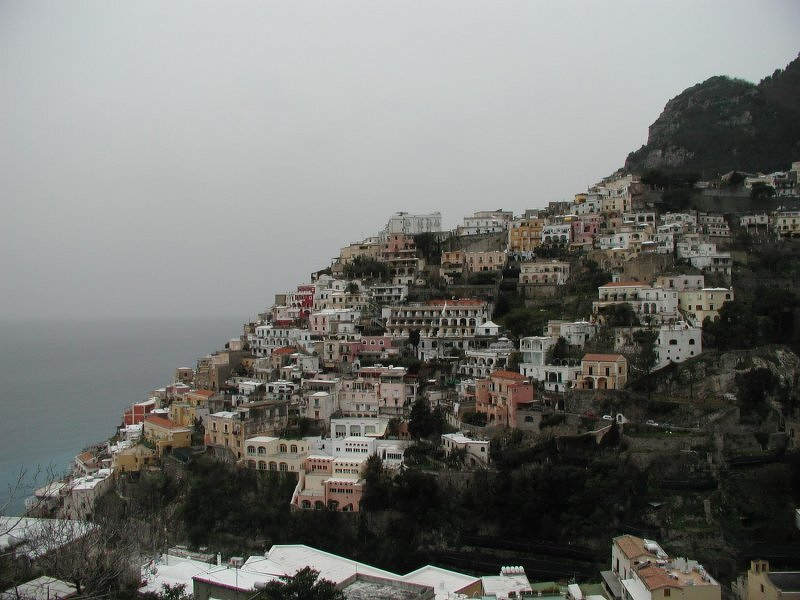 A collection of colourful houses cling to a steep hillside above the sea in Italy