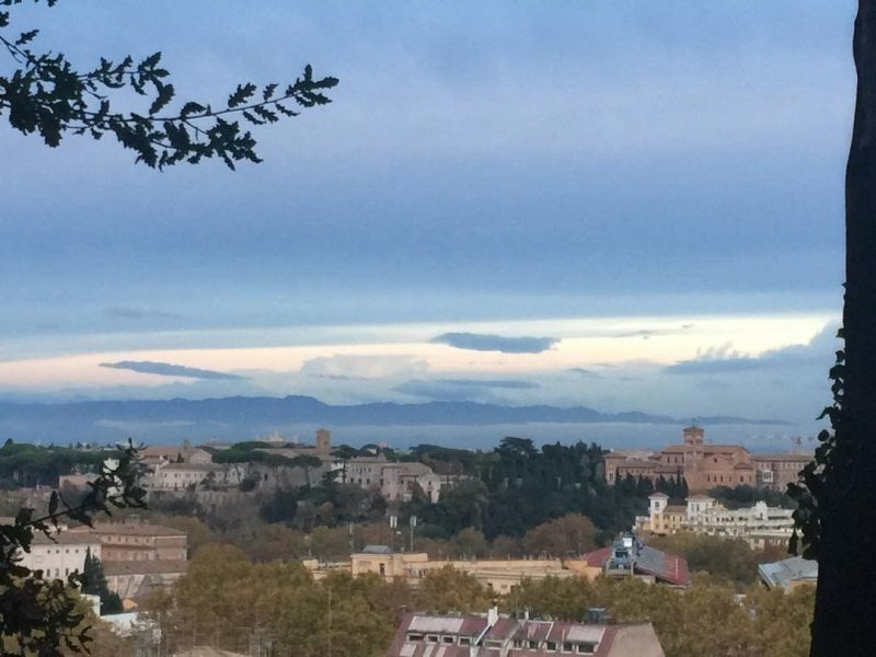 Auto-generated description: A scenic view of a cityscape with a mix of historical buildings and lush greenery, set against a backdrop of distant mountains and a cloudy sky.