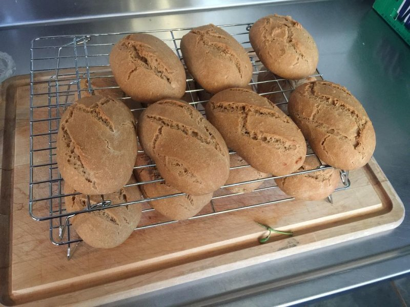 Auto-generated description: Several loaves of crusty bread are cooling on a wire rack placed on a wooden cutting board.