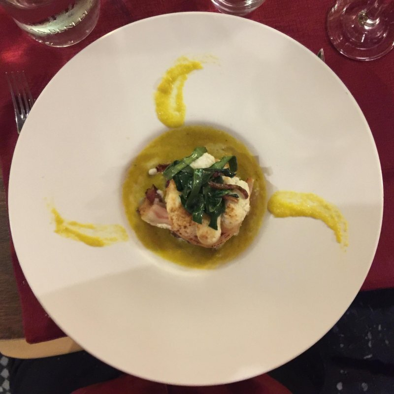 Auto-generated description: A gourmet dish is elegantly plated with a piece of meat, greens, and a yellow sauce, surrounded by artistic sauce presentation.