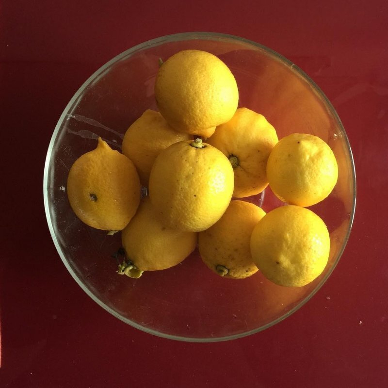Auto-generated description: A clear bowl filled with yellow lemons sits on a red surface.