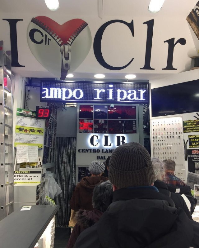 Auto-generated description: People are standing in line inside a shop with signage.