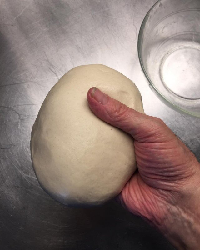 Auto-generated description: A hand is holding a smooth, round ball of dough over a metallic surface.