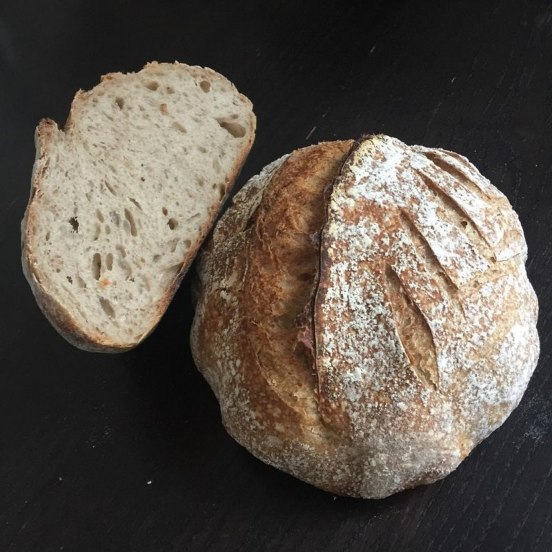 Auto-generated description: A sliced loaf of crusty sourdough bread rests on a dark surface, showcasing its airy interior and textured exterior.