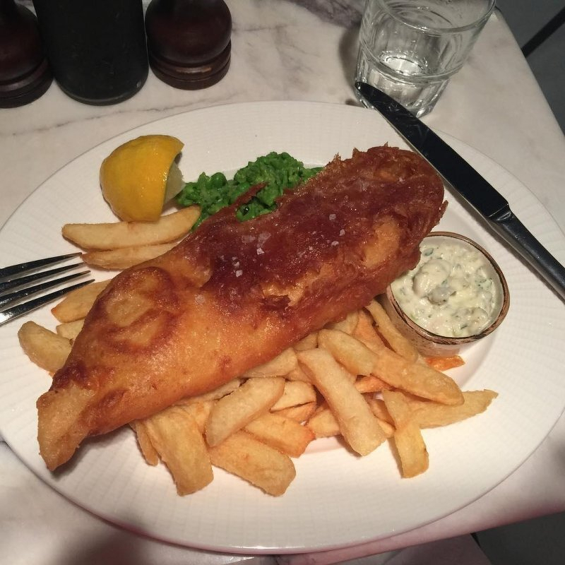 Auto-generated description: A plate of fish and chips with mushy peas, a lemon wedge, and a small serving of tartar sauce.