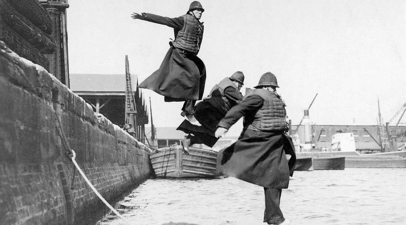 Auto-generated description: Three individuals in uniforms practice jumping onto a boat docked in a harbor.