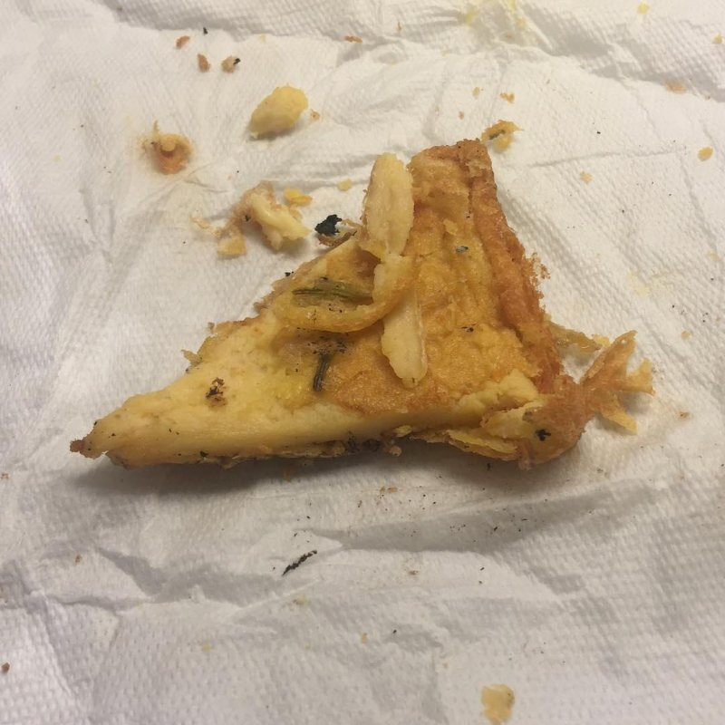 Auto-generated description: A piece of farinata di ceci with topping of onions sits on a crumpled paper towel.