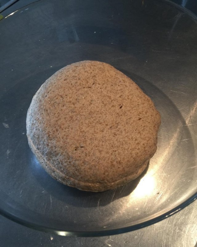 Auto-generated description: A ball of dough sits in a glass bowl on a metallic surface.