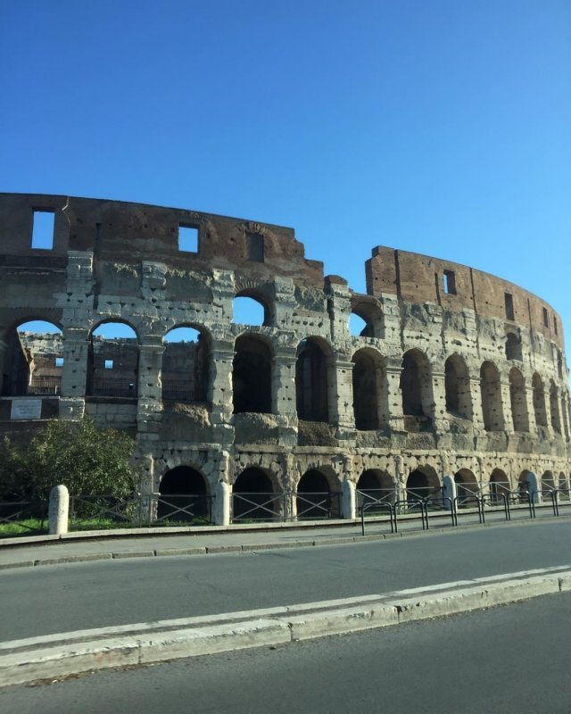 Auto-generated description: A large, ancient amphitheater with arched walls, the Collosseum, stands under a clear blue sky.