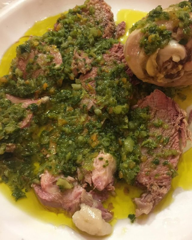 Auto-generated description: Slices of cooked meat are covered in a green herb sauce on a white plate.