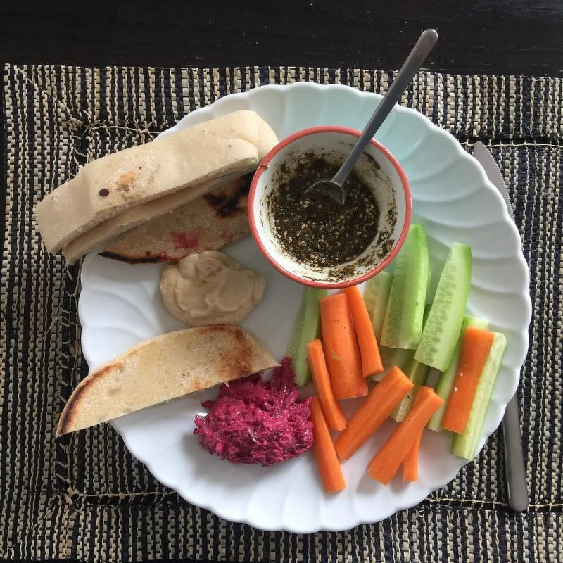 Auto-generated description: A plate of carrot and cucumber sticks, bread with spreads, and a bowl containing a green seasoning mix.