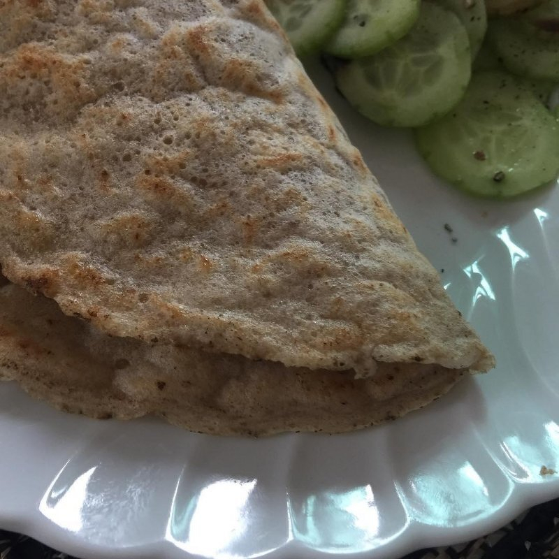 Auto-generated description: A folded pancake is placed on a white plate alongside sliced cucumbers.