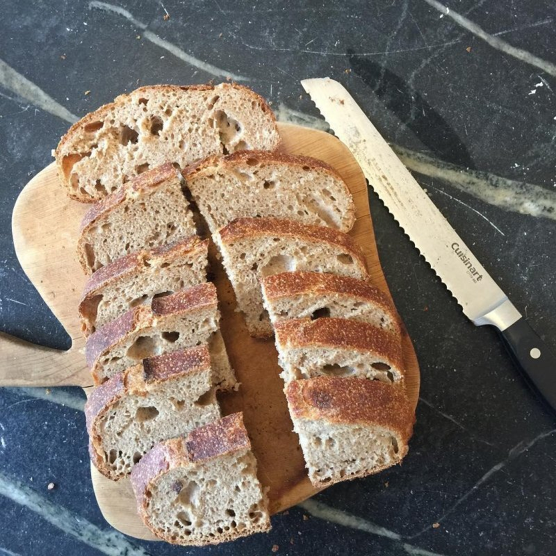 Auto-generated description: A loaf of sliced whole grain bread is on a wooden cutting board next to a serrated knife.