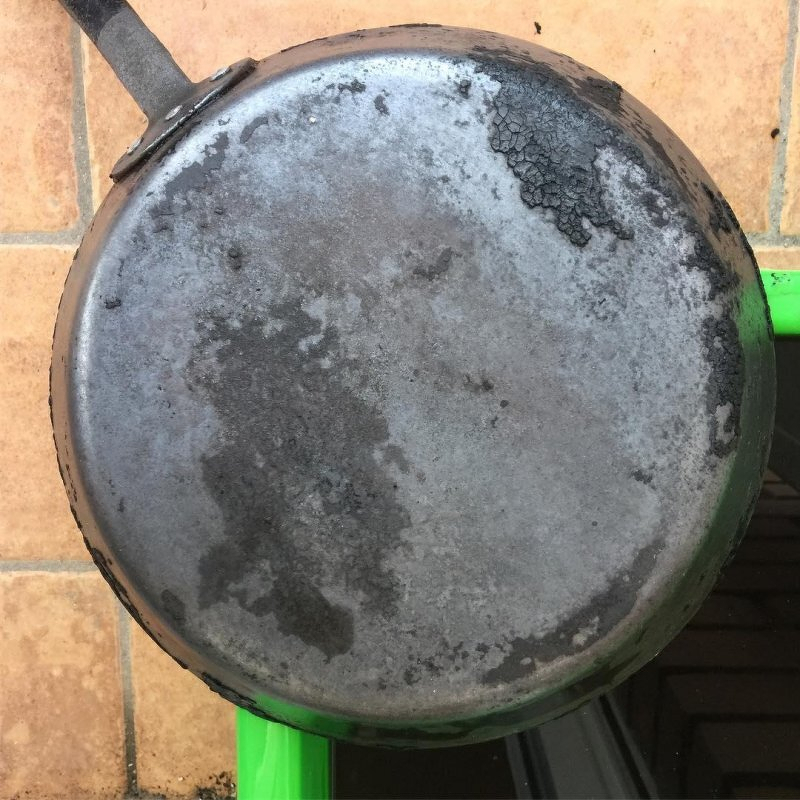 Auto-generated description: A cast-iron frying pan with patches of rust and discoloration is resting on a tiled surface.