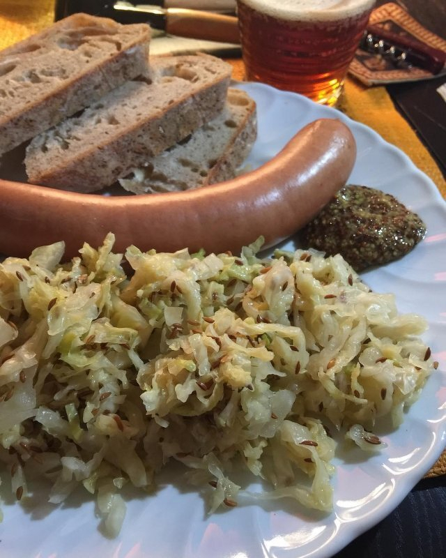Auto-generated description: A plate features a sausage, mustard, sauerkraut, and slices of bread.